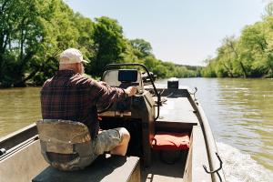 Older man drives a fishing boat upriver near Brookneal