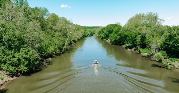Bass boat glides down brown river with trees on both sides