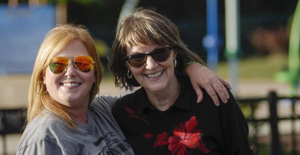 Two ladies in sunglasses smile into camera and hug