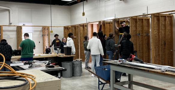 A group of students in an electrical lab watch as a student installs conduit