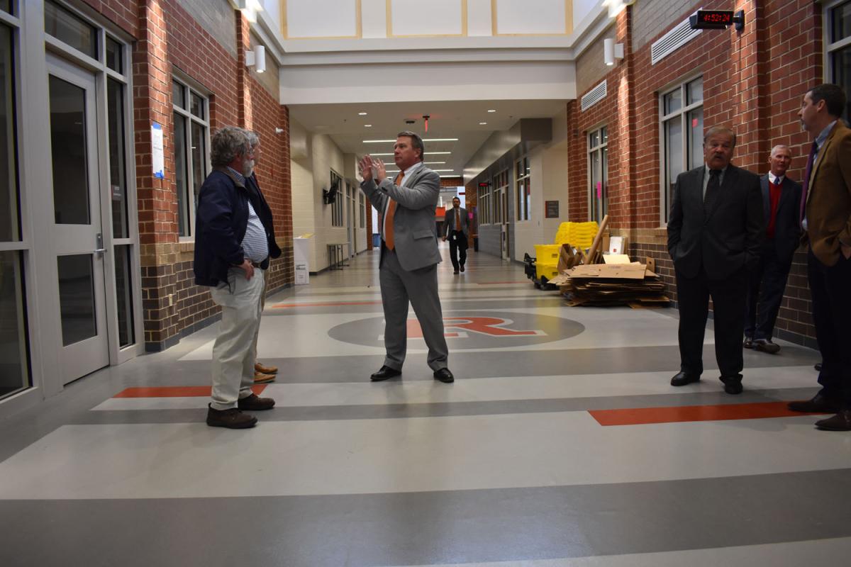 Superintendent Johnson stands in the main hallway with tour participants. A pile of cardboard sits in the background along wall