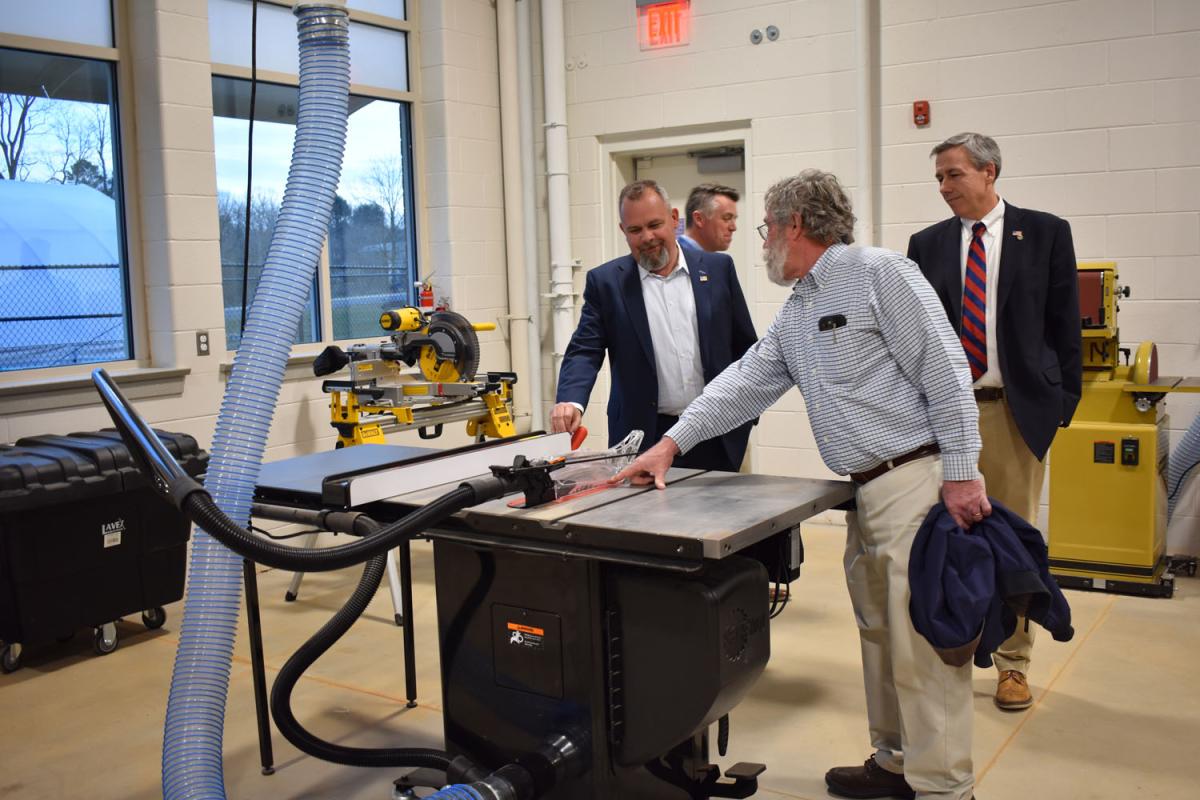 Three men look at table saw in shop class
