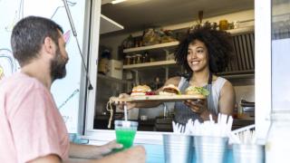 woman in a food truck window smiles and hands order to customer