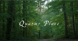 Atmospheric photo of woods with filtered light flowing through the trees and the words "Quarter Place" centered in white letters